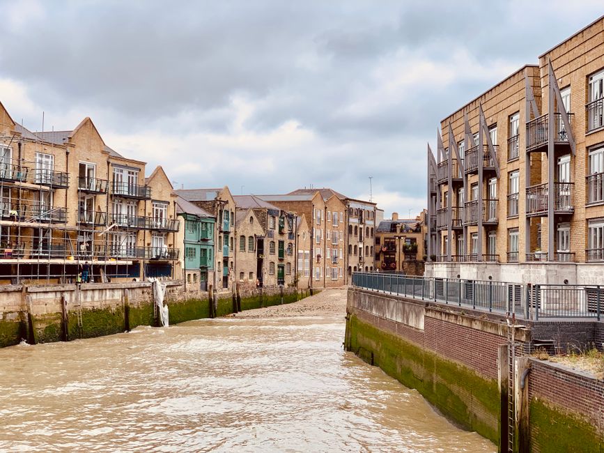 A street scene in Limehouse featuring a large, brick-built building with arched windows on the left and a blue railway bridge with yellow lettering reading 'CADDIN LOCK' spanning across the road. The