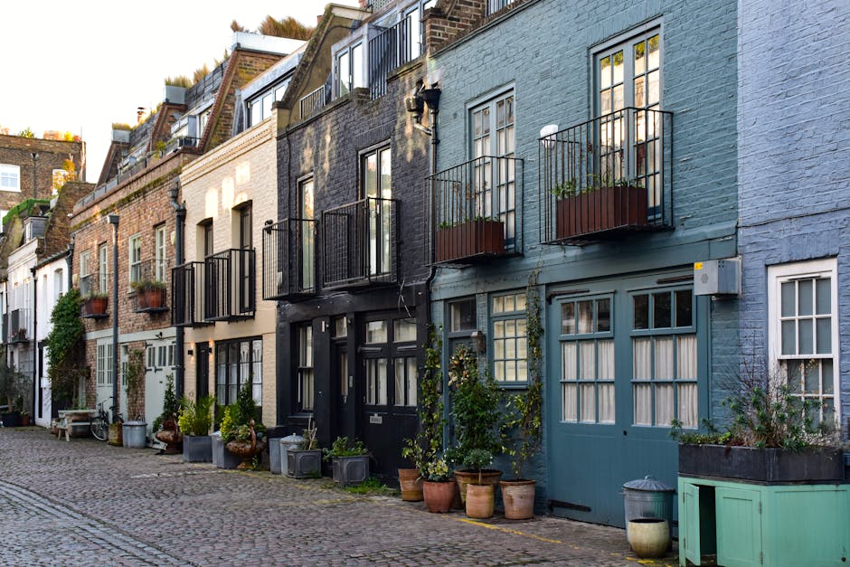 The image depicts a narrow cobblestone street lined with multi-storey brick buildings on both sides, featuring external fire escape staircases and small balconies. The buildings' facades include large